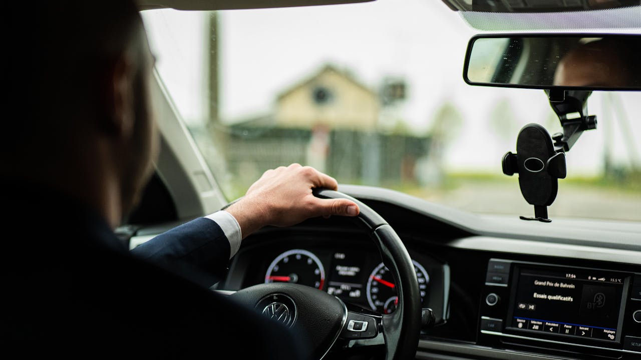 Businessman in suit driving a car, focus on steering wheel and dashboard.